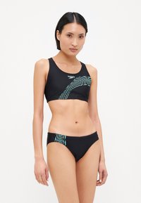 Zwart zwemtop en bikinitop met een turquoise golfpatroon. De top heeft een racerback ontwerp; de onderkant is low-rise.