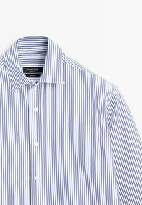 Hvid skjorte med tynde, lodrette blå striber, knappet foran, udbredt krave og et synligt mærke indeni kraven.