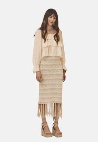 Blusa beige con volantes en capas combinada con una falda tejida de tonos pasteles con dobladillo desflecado. Las sandalias de cuña completan el conjunto.