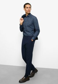 Marineblaue, gemusterte Hemdjacke mit langen Ärmeln, kombiniert mit marineblauen Hosen und braunen Loafers. Das Hemd zeichnet sich durch ein dezentes mehrfarbiges Design aus.