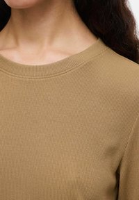 Rękawowy sweter z prążkowanej tkaniny w jasnobrązowym kolorze, z szerokim dekoltem i miękką strukturą, widoczne szwy wzdłuż brzegów.