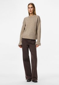 Beige kötött pulóver hosszú ujjal és bordázott aljjal, laza barna nadrággal párosítva. Simaszerkezet és laza fazon.