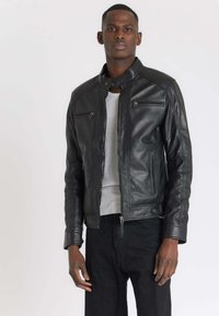 Veste en cuir noir avec col, fermeture éclair à l'avant et plusieurs poches zippées. Texture lisse avec une coupe ajustée.