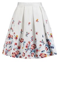 Jupe blanche avec des motifs floraux colorés en rouge, jaune et bleu. Présente des plis et une taille ajustée, fabriquée en tissu léger.