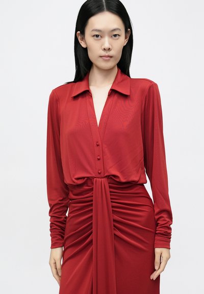 Piros, hosszú ujjú ruha gallérral, gombos elülső résszel, összehúzott derékkal és sima, folyékony anyagtextúrával.