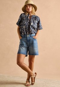 Halenka s kvetinovým vzorom v námorníckej modrej farbe s výstrihom v tvare kľúča, spárovaná so svetlomodrými džínsovými šortkami. Vzhľad dopĺňajú béžové sandále a slamenný klobúk.