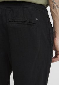 Pantalons en lin noir avec une coupe décontractée, dotés d'une poche arrière et de détails de couture subtils. La texture semble légère et respirante.