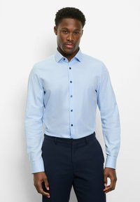 Hellblaues, langärmliges Hemd mit Knöpfen, figurbetontem Schnitt, dunklen Knöpfen und klassischem Kragen, getragen zu dunklen Hosen.