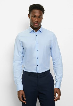 Hellblaues, langärmliges Hemd mit Knöpfen, figurbetontem Schnitt, dunklen Knöpfen und klassischem Kragen, getragen zu dunklen Hosen.