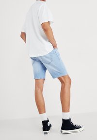 Shorts de denim azul claro con un corte relajado, dos bolsillos traseros y dobladillos enrollados. Combinados con una camiseta blanca y zapatillas altas negras.