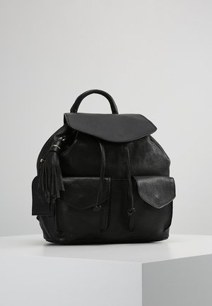 Czarny skórzany plecak z przednią klapą, dwoma przednimi kieszeniami z klapami, zapięciem na sznurek, górnym uchwytem oraz skórzaną ozdobą z frędzlami na białym tle.
