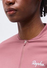 Κοντινό πλάνο στο κάτω μέρος του προσώπου και στον λαιμό ενός ατόμου που φοράει ένα ζιπ-απ μώβ ποδηλατικό μπλουζάκι Rapha.