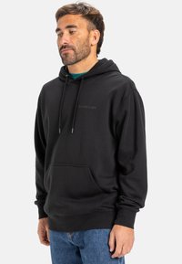 Black hoodie made of cotton blend fabric, featuring a front kangaroo pocket, drawstring hood, and logo on the chest. Casual fit.