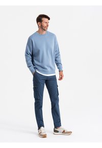 Błękitny sweatshirt z okrągłym dekoltem, sparowany z ciemnoniebieskimi spodniami cargo z bocznymi kieszeniami. Całość dopełniają białe i szare sneakersy.