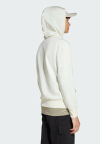 White hooded sweatshirt with a soft texture, matched with a beige undershirt, and black cargo pants. Features ribbed cuffs and hem.