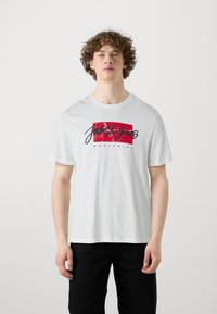 T-shirt bianca in cotone con un logo grafico rosso e nero, collo rotondo, maniche corte e vestibilità rilassata. Il testo recita "Jack & Jones Worldwide."