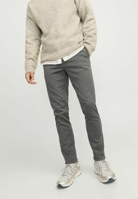 Pantalones gris ajustados combinados con un suéter de punto beige, superpuesto a una camisa blanca de botones. El atuendo se completa con zapatillas claras.