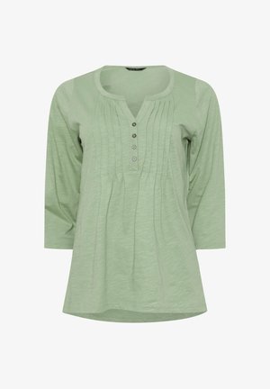 Camicia lunga a maniche lunghe verde chiaro con scollo rotondo, pattina con quattro bottoni e pieghe verticali lungo il davanti.