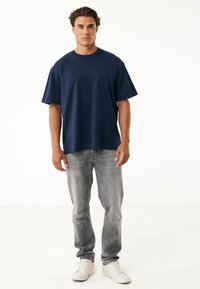 Camiseta de algodón azul marino con un corte relajado, mangas cortas y escote redondo, combinada con jeans gris claro y zapatillas blancas.