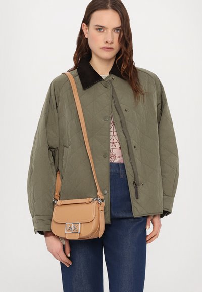 Quilted olivgrüne Jacke mit einem schwarzen Kordkragen, kombiniert mit einer braunen Umhängetasche mit silbernem Logo und Schultergurt.