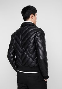 Zwarte leren jas met een chevron-quiltpatroon, ribbelmanchetten en kraag, met een soepele textuur en een getailleerd ontwerp.