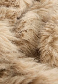 Blødt faux fur tekstil i beige, der har en fluffy tekstur med lange fibre, som viser variationer i nuancer og dybde.