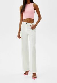 Ljusrosa ribbad crop top, högmidjade vita byxor och rosa remsandaler. Har en slim fit och kort design.