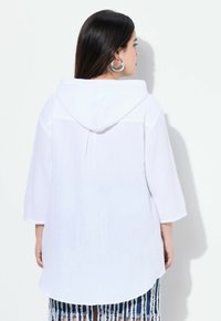 Camicia bianca in cotone con cappuccio, maniche a tre quarti, tessuto texturizzato e orlo arrotondato. Presenta una vestibilità ampia e un look a strati.