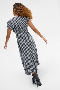 Μαύρο και λευκό καρό φόρεμα με κοντά μανίκια, εφαρμοστή μέση και μακριά, ρέουσα φούστα· συνδυασμένο με μαύρα μποτάκια μέχρι τον αστράγαλο με διακοσμητικά στοιχεία.