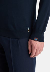 Suéter azul marino con tejido texturizado, puños acanalados y tres costuras decorativas en azul claro y beige en el dobladillo.