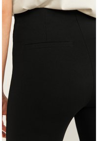 Zwarte legging met een gladde textuur, voorzien van een achterzak en een aansluitend ontwerp. De tailleband is elastisch voor extra comfort.