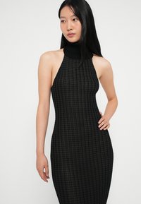 Μαύρο ριγέ φόρεμα με ψηλό γιακά και χωρίς μανίκια; η εφαρμοστή γραμμή τονίζει τη σιλουέτα. Υφασμάτινο μοτίβο σε όλη την επιφάνεια.