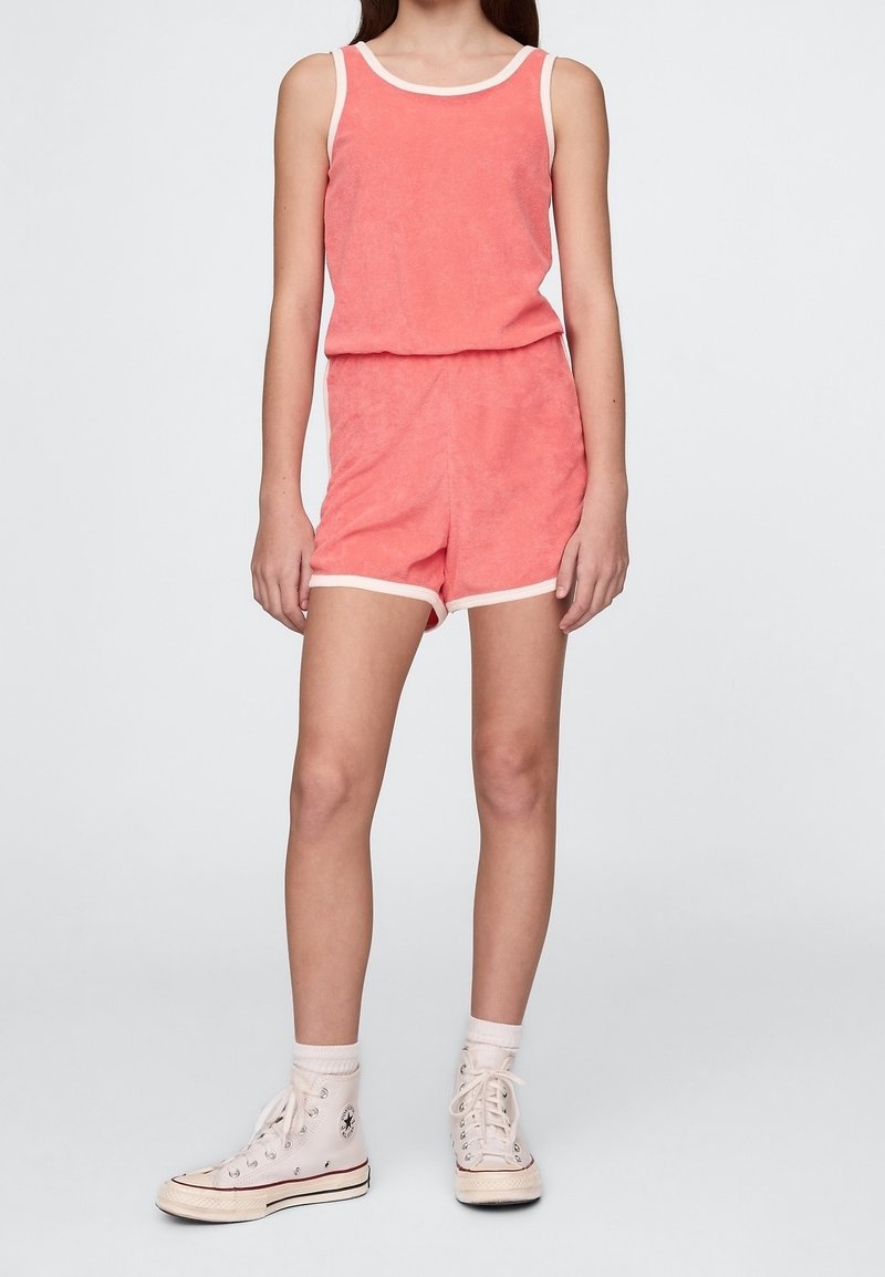 Jeune personne portant un débardeur en éponge corail et un short assorti avec bordure blanche, des chaussettes blanches montantes et des baskets blanches montantes.