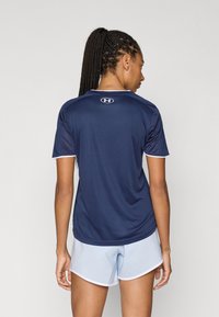 Tengerészkék sportpóló rövid ujjakkal és kerek nyakkivágással, világoskék díszítésekkel és az Under Armour logóval a háton.