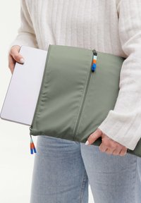 Funda acolchada verde para laptop con doble cremallera, acentos de hardware coloridos y una textura suave. Acomoda de forma segura una tableta o un laptop pequeño.