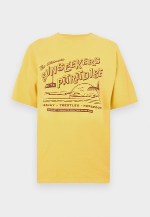 Yellow cotton t-shirt featuring a graphic design with text "Sunseekers Paradise" and beach elements. Short sleeves and a round neckline.