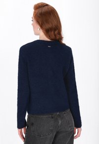 Maglione lavorato a maglia blu navy con finitura testurizzata, maniche lunghe e scollo rotondo. Presenta un piccolo logo metallico sulla parte posteriore.