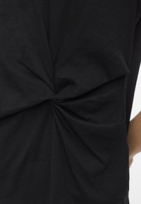 Camiseta negra de algodón suave, con un detalle de nudo torcido en la parte trasera. Diseño sencillo con mangas cortas y un ajuste relajado.