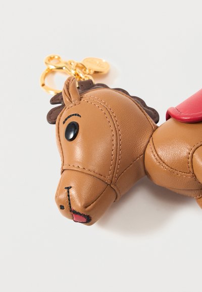 Barna bőrből készült ló kulcstartó fekete szemekkel, varrott arcvonásokkal, piros nyereggel és arany fém kulcskarika fehér háttéren.