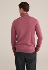 Dolgi rokav, roza turtleneck pulover iz mehkega materiala, z rebrastimi manšetami in robom, v kombinaciji s temnimi hlačami. Minimalističen dizajn.