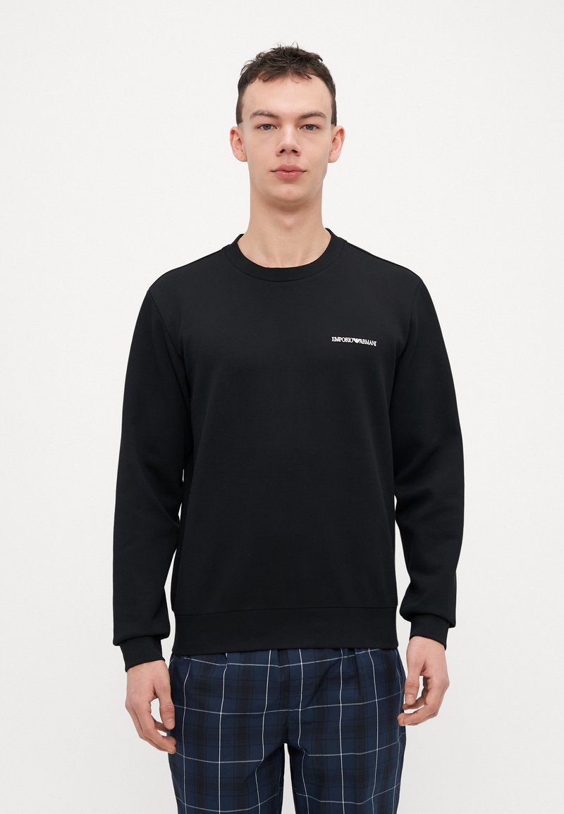 Sweatshirt noir avec manches longues, encolure ronde et poignets côtelés. Présente un petit logo "Emporio Armani" blanc sur la poitrine.
