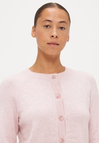 Jasnoróżowy kardigan z okrągłym dekoltem, długimi rękawami i pięcioma guzikami z przodu. Miękka tekstura z prążkowanymi akcentami.