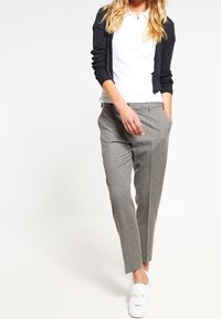 Grå skräddarsydda byxor med slim fit, slät textur, veck framtill, parat med en vit polo och en svart cardigan, kompletterat med vita skor.