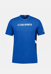 Camiseta azul con "LE COQ SPORTIF" impreso en blanco, de mangas cortas, cuello redondo, con paneles laterales en navy y un acento de logo en la manga.