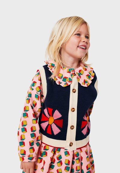 Cardigan azul marino con un gran diseño de flores, tapeta de botones beige, y blusa con cuello rosa en contraste que presenta patrones de cubos coloridos.