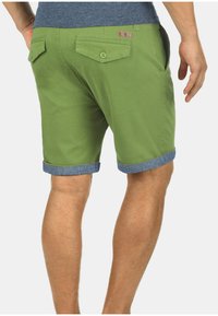 Groene katoenen shorts met een opgerolde denim zoom, voorzien van twee achterzakken met knoopsluiting en een klein merklabel op de tailleband.