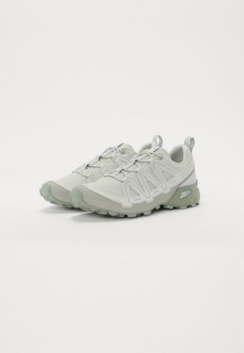 Zapatillas deportivas de color gris claro con una parte superior de malla texturizada, suela de goma en forma de garra y un patrón decorativo superpuesto para mayor soporte.