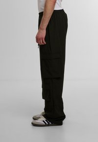 Svarte cargo-bukser med elastisk midje, flere sidelommer og løs passform. Brukt med hvite og grå sneakers.