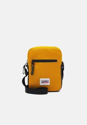 Sac bandoulière jaune avec poche zippée noire, sangle noire réglable et patch logo blanc Tommy Jeans à l'avant.