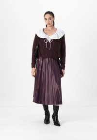 Bordo pulover z velikim belim ovratnikom, belim trakom za zapiranje; nabran vijoličen krilo; črne škornje do kolen; mala črna torbica.